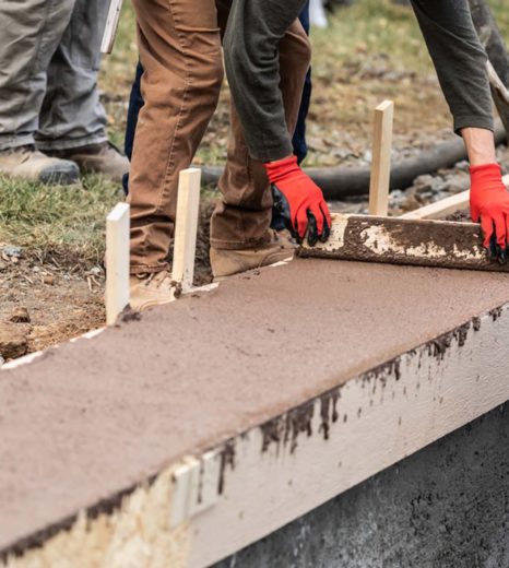 Construction Workers Pouring And Leveling Wet Cement Into Wood Framing - Turnkey Pool Designers