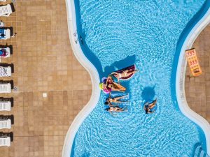 Aerial vertical view of group of women friends have fun together in summer holiday vacation at pool resort with coloured inflatables lilos on the blue water