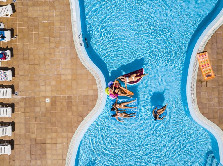Aerial vertical view of group of women friends have fun together in summer holiday vacation at pool resort with coloured inflatables lilos on the blue water