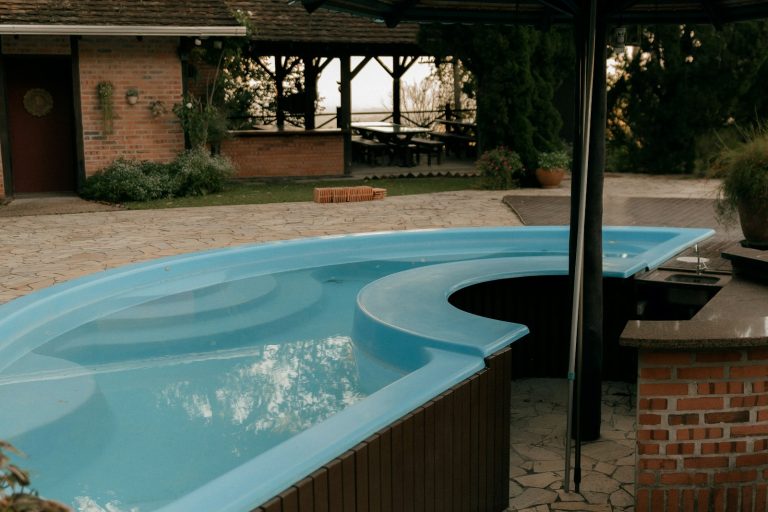 Fiberglass shell pool with curved steps beside a brick outdoor kitchen and patio