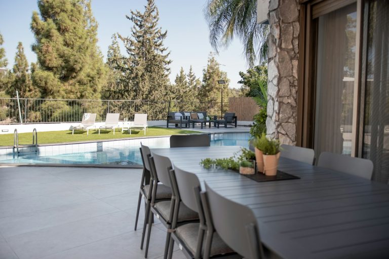 Poolside dining table and lounge chairs beside a backyard pool, showing outdoor living costs beyond the pool