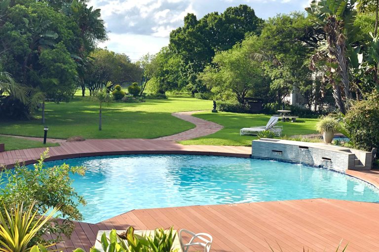 Freeform backyard pool with a stone water feature wall and timber deck in a landscaped garden