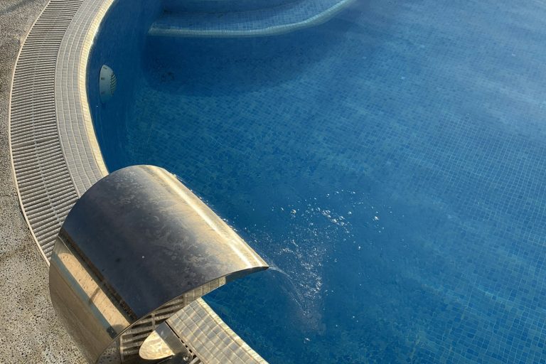 Pool with a stainless sheer descent water feature spilling into blue mosaic tiled water