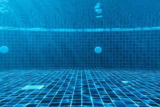 Underwater view of a blue tiled pool interior showing the surface and fittings