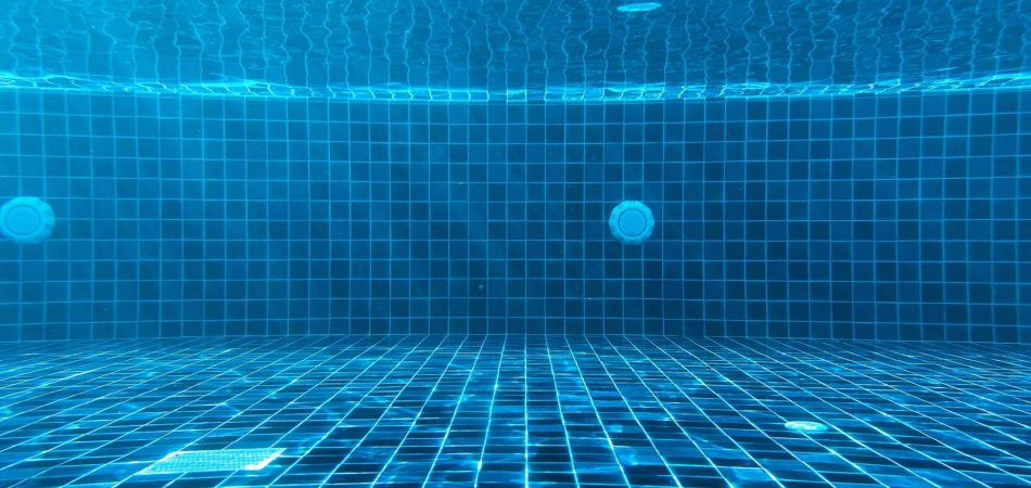 Underwater view of a blue tiled pool interior showing the surface and fittings
