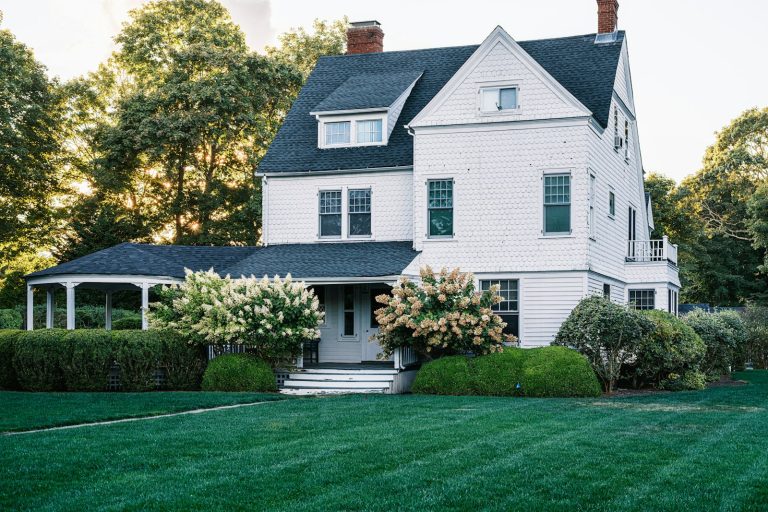 White clapboard home with a wide lawn and mature planting on a summer evening