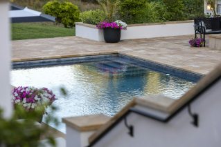 Backyard pool with travertine coping and planted borders on a calm evening