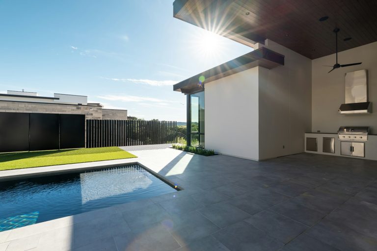 Backyard pool beside a covered patio and outdoor kitchen, showing the full scope of a finished project