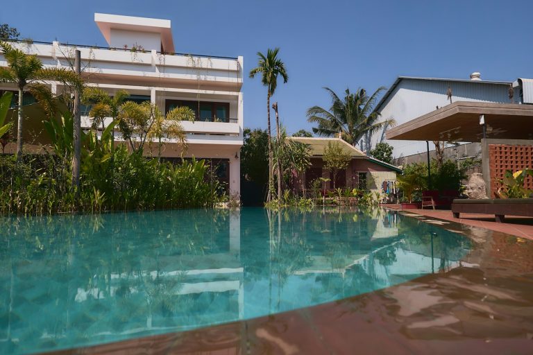 Swimming pool with palms and a two-storey home beyond on a clear day
