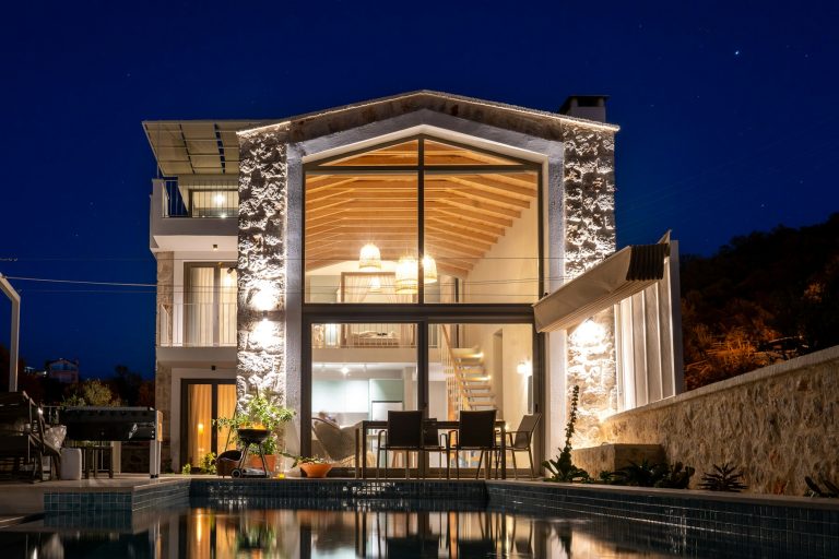 Home with a lit swimming pool and covered seating in the evening