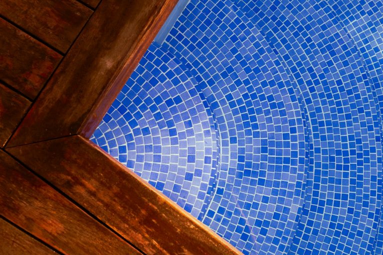 Timber deck boards meeting blue mosaic pool tile at the pool edge