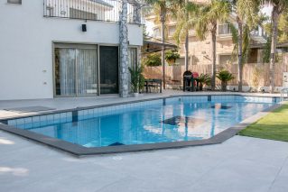 Backyard swimming pool beside a white two-storey home with palm trees