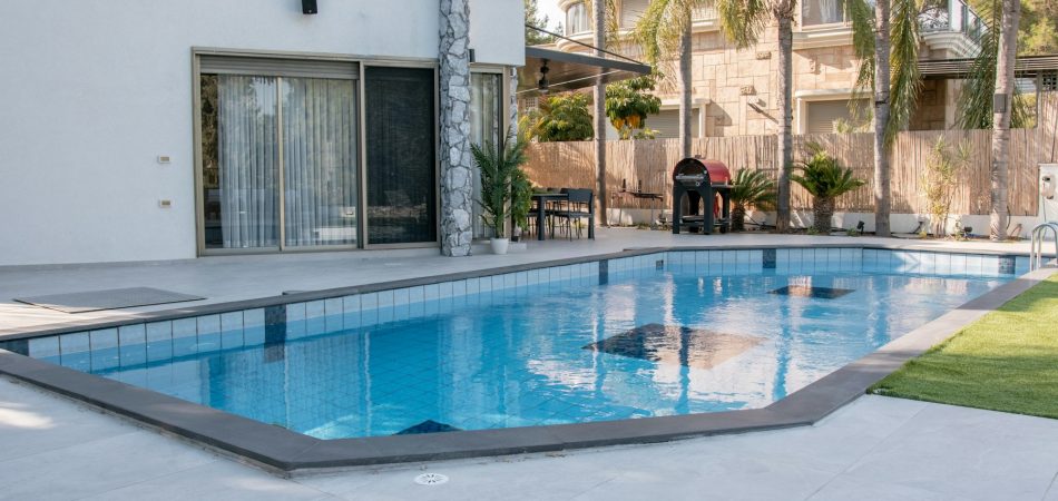 Backyard swimming pool beside a white two-storey home with palm trees