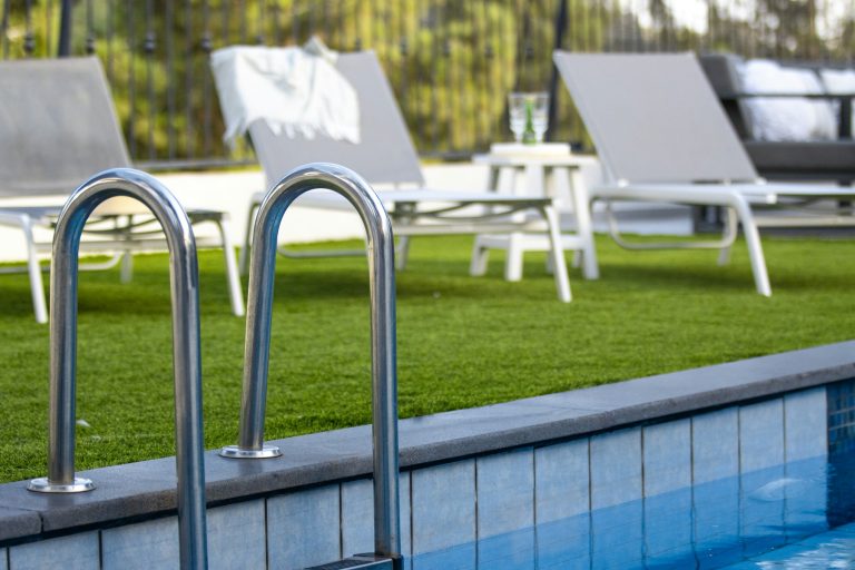 Pool ladder and lounge chairs on a lawn beside a full swimming pool