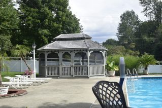 Fenced backyard pool area with a wooden gazebo and lounge chairs
