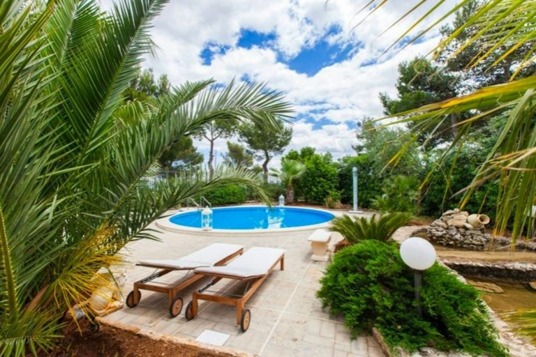 Two wooden lounge chairs on a stone patio beside a round swimming pool