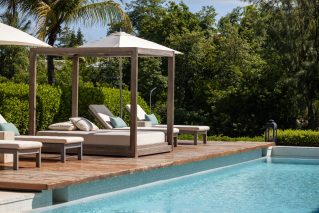 Timber cabana with cushions beside a swimming pool in a garden