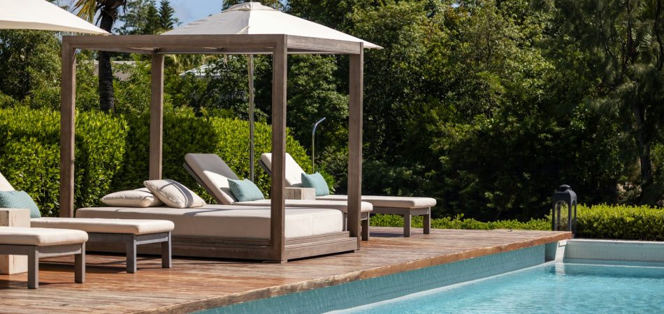 Timber cabana with cushions beside a swimming pool in a garden